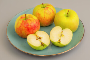 Red apples with green whole and cut in half in a plate on a gray background. Apple, vitamin