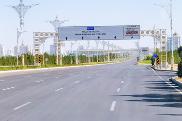 Wide boulevard in Ashgabat with decorative streetlights and lush greenery on both sides, showcasing modern urban infrastructure. Turkmenistan