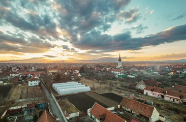 Obraz premium Captivating sunset envelops Rasnov with vibrant colors illuminating the rooftops. The nearby mountains add a majestic backdrop to this serene landscape, showcasing nature's beauty