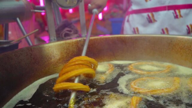 Removes freshly fried churros from the hot oil, observing their golden color and crunchy texture.