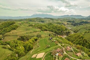 Fototapeta premium Expansive green hills roll across the landscape, dotted with quaint homes and farmsteads in the Piatra Craiului area