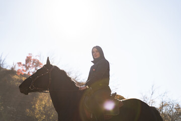 An attractive brunette female equestrian riding a black horse in the countryside on a sunny autumn...