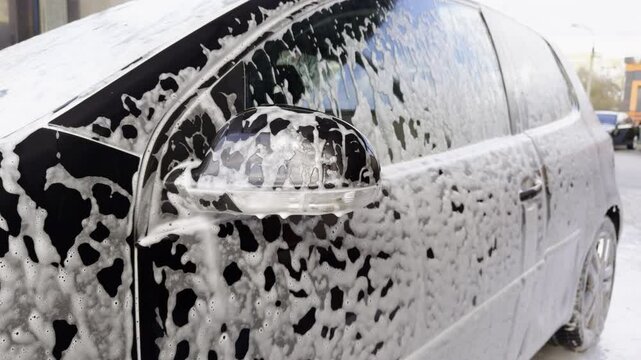 Close-up image of details from a car wash. Black car full of detergent on the outside specially for cleaning cars. The process of professional cleaning of a car at a reputable car wash