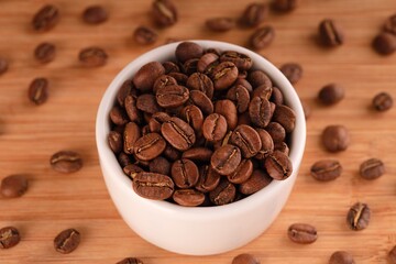 Coffee beans in a small white bowl on a wooden background near other coffee beans.