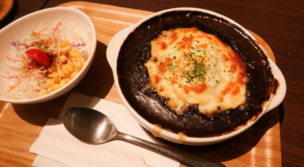 close up of baked Japanese curry with cheese on top on a plate with salad on the side on a wooden tray