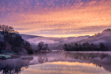 Stunning beautiful Autumn sunrise atmospheric landscape image of Rydal Water in Lake District with unbelievable colours in low level mist over lake