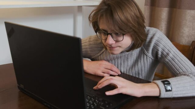 Young man wearing glasses focuses intently on a laptop, browsing the internet in a slow motion setting