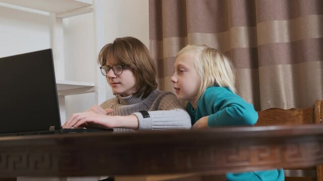 Older brother assisting younger brother with laptop in slow motion, showcasing a moment of learning and connection