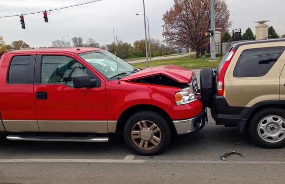 Rear-end vehicle collision involving red truck with bent hood and brown suv