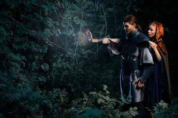 A knight and cloaked woman explore an enchanted forest, casting a magic, glowing with magical...