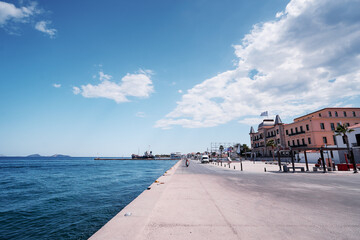 Travel by Greece. A scenic coastal promenade with a clear blue sky, calm sea, and historic...