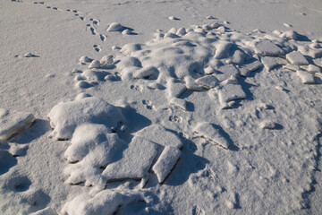 There are many broken pieces of ice covered with snow on the ice, the snow glitters.