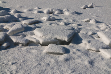 There are many broken pieces of ice covered with snow on the ice, the snow glitters.