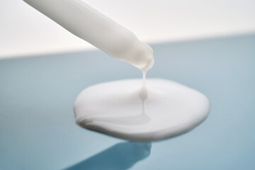 Pipette with white cream serum on blue background.