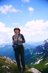 a young girl with a backpack stands and smiles against the background of mountains and nature