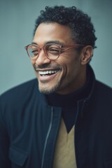 Obraz premium A man with glasses is smiling and wearing a black jacket and a brown sweater. Concept of warmth and happiness, as the man is enjoying himself