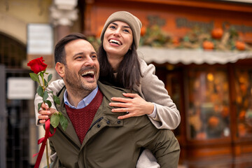 Mid adult Caucasian male carrying girlfriend in cozy winter attire, holding a rose on Valentines Day.