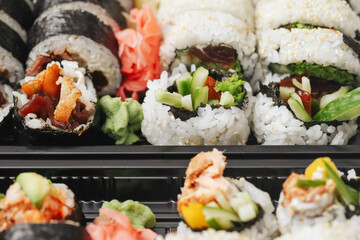 Sushi assortment in a black takeaway box. Closeup of California rolls, futomaki, and uramaki. Fresh Japanese cuisine with sesame seeds and colorful toppings. Lunch or dinner sushi to-go option.