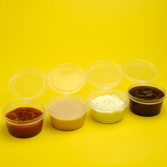 Four different sauces in jars for seasoning meat on a yellow background. Mayonnaise, ketchup, sauce.