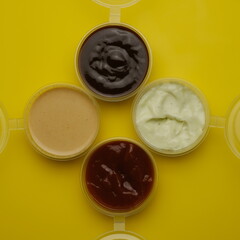 Four different sauces in jars for seasoning meat on a yellow background. Mayonnaise, ketchup, sauce.