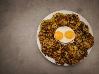 Zucchini and carrot pancakes with fried eggs on a white plate