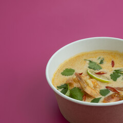 Asian Tom Yum soup on pink background.