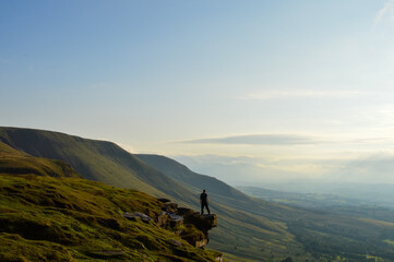 A man standing back to camera on an escarpment in the mountains. Brecon Beacons Wales, UK