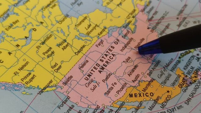 Closeup of pen tip touching United States of America county location or territory mark drawing on a map with some USA city name word or text written on the surface. Travel tourism creative concept.