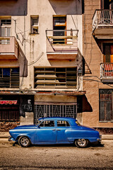 A blue car is parked on a city street in front of a building