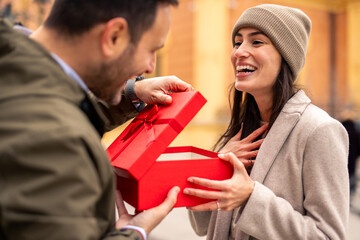 A cheerful Caucasian couple shares gifts on International Women's Day. Both dressed in stylish...