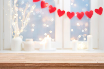 Empty wooden table top on blurred window interior decorated with red heart garland of valentine day celebration