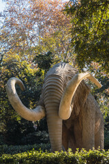Life-sized mammoth statue surrounded by trees in park