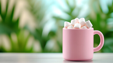 Pink mug filled with fluffy marshmallows against a blurred green background, offering a cozy and sweet treat.