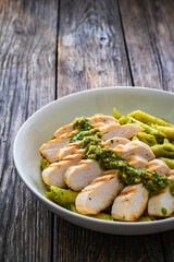 Penne with basil pesto sauce and grilled chicken breast on wooden table	