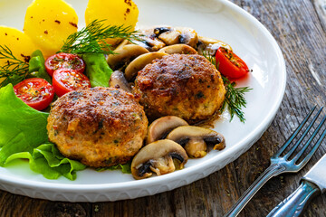 Fried pork meatballs with boiled potatoes and fried mushrooms on wooden table