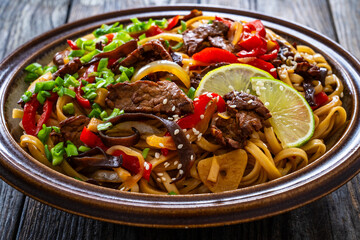 Asian style stir fried vegetables, roast beef and chow mein noodles on wooden table	