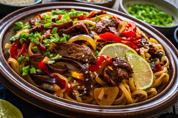 Asian style stir fried vegetables, roast beef and chow mein noodles on wooden table	