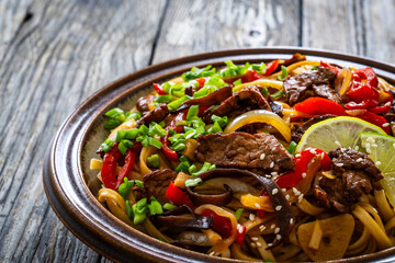 Asian style stir fried vegetables, roast beef and chow mein noodles on wooden table	