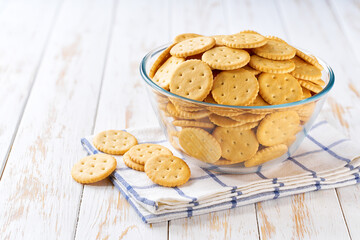 Traditional round crackers in a clear glass bowl with on a light kitchen table, selective focus.