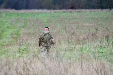 British army male soldier tabbing with 25Kg bergen through a winter grass meadow, Wiltshire UK