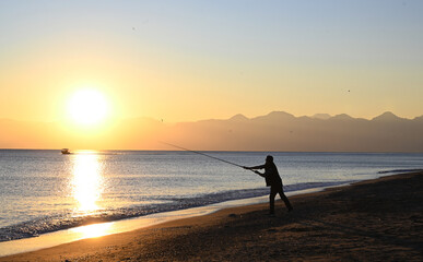 Fototapeta premium People fishing with fishing rods from the beach at sunset