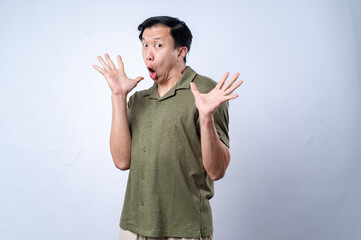 An Asian man in a green polo shirt reacts with an exaggerated surprised expression, raising both hands near his face, conveying excitement or shock, against a plain white background