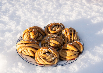 Floral plate with festive swedish pastries, homemade cinnamon rolls. Resting on fresh white snow in the morning sun