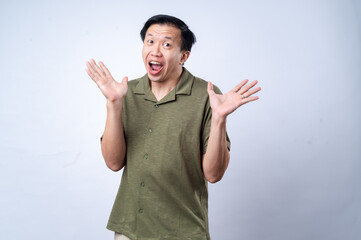 An Asian man in a green polo shirt reacts with an exaggerated surprised expression, raising both hands near his face, conveying excitement or shock, against a plain white background