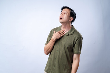 A concerned man in a casual green shirt is depicted holding his throat, appearing uncomfortable, in front of a plain light blue background. The image conveys discomfort or health issues