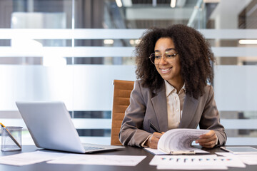 A young African American woman works in the office at a desk, conducts a video conference, makes...