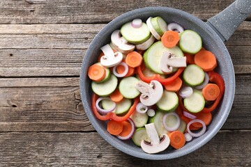 Frying pan with mix of fresh vegetables and mushrooms on wooden table, top view