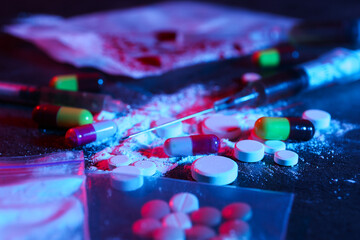 Drug addiction. Different pills, powder and syringe on dark table in neon lights, closeup