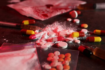 Drug addiction. Different pills, powder and syringes on dark table in color light, closeup