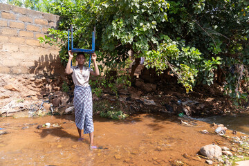 Young African girl carries furniture from her flooded parents' house on her head to save her...